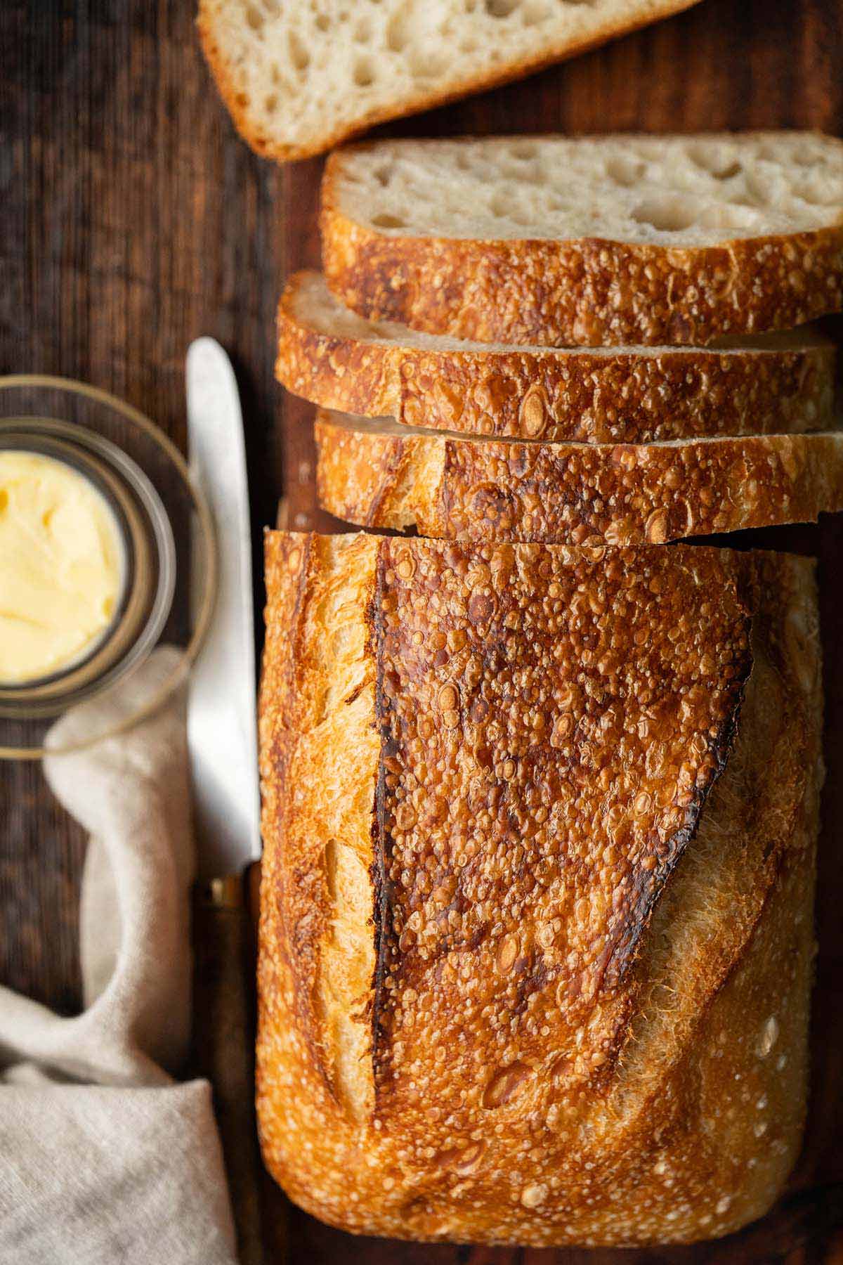 top view of crusty loaf of sourdough bread with blistered golden crust on vintage wooden table